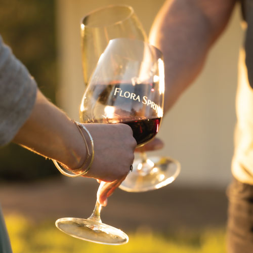 Two people cheers with red wine from Flora Springs.